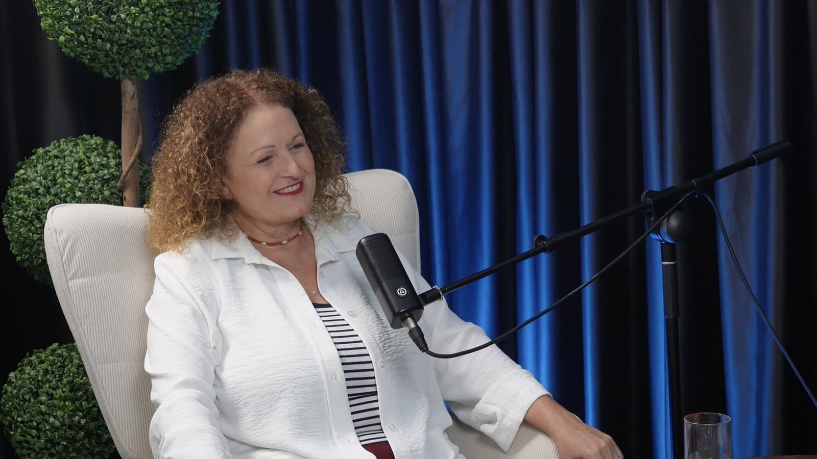 דורית גבאי באולפן הבונקר: כורסה לבנה, מיקרופון ווילון מואר בכחול